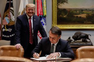 Jair Bolsonaro signing a document at the White House as President Trump stands behind, smiling