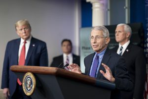Dr. Anthony Fauci speaking at a podium with Donald Trump and Mike Pence in the background