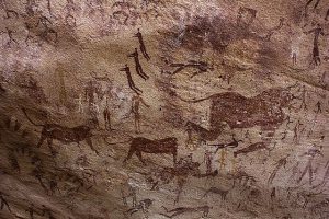 A photograph of prehistoric cave drawings of humanlike figures dancing, floating and swimming around beasts