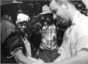A white man drawing blood from a Black man during the Tuskegee Syphilis Study
