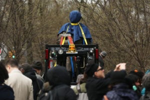 The statue of Sims covered in a blue cloth amongst cameras and a crowd of people