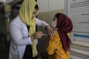 A woman in a white coat administering a vaccine to a child wearing a mask