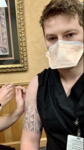 Alex Campbell wearing a mask and receiving a vaccine