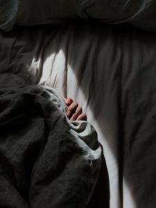 A hand peeking out from under the bed sheets in a dark room