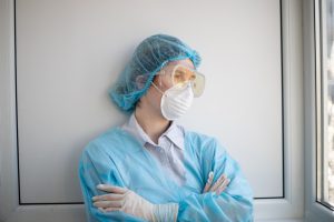 A medical professional stands with arms crossed against a wall, gazing out the window