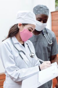 A female doctor in a white coat writing something and a black male medical student