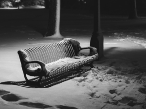 A black and white photograph of the disheveled snowy ground next to a bench