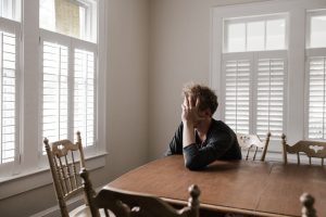 A white male student sitting at a dining table and holding his head