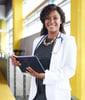Doctor in her white coat in a hospital setting, holding her tablet and smiling at the camera