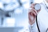 Medical student holding up stethoscope with operating room faded in the background