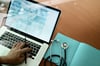 A Dr's hand using laptop with stethoscope next to the laptop